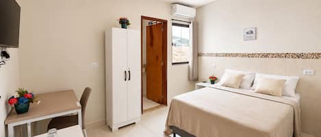 Una habitación de hotel con cama, escritorio, armario y aire acondicionado.