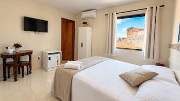 Una habitación de hotel con cama, escritorio, televisor y ventana con cortinas.