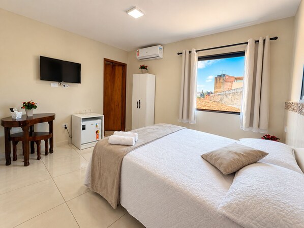 A hotel room with a bed, a desk, a TV, and a window with curtains.