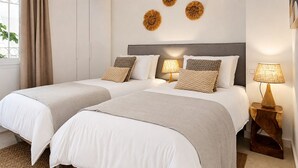 A hotel room with two beds, a window with curtains, wall-mounted lamps, and decorative wall art. - Beautiful apartment with pool & sea views (Mijas Costa)