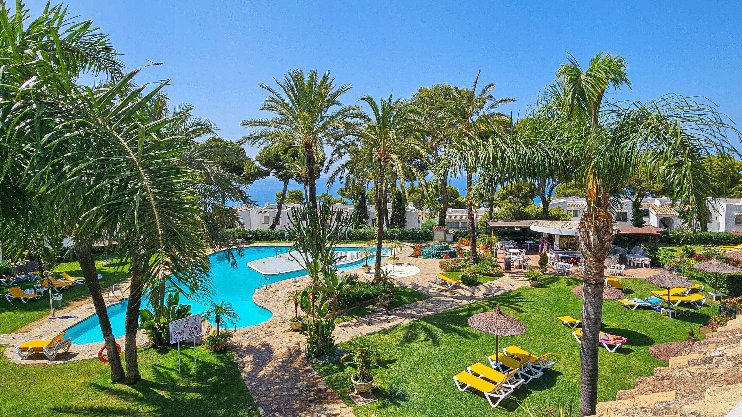 A resort with a swimming pool, palm trees, and outdoor seating areas.
