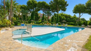 A swimming pool with a stone deck, surrounded by palm trees and lounge chairs. - Beautiful apartment with pool & sea views (Mijas Costa)