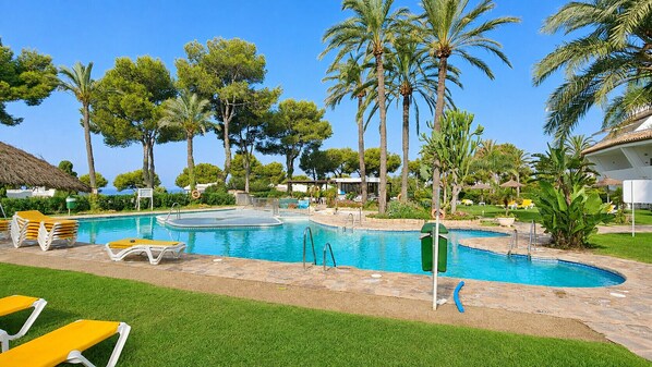 A swimming pool with multiple lanes, surrounded by palm trees and lounge chairs. - Beautiful apartment with pool & sea views (Mijas Costa)