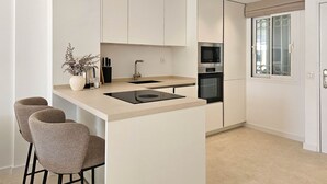 A modern kitchen with a central island, bar stools, a built-in oven, and a window with decorative glass. - Beautiful apartment with pool & sea views (Mijas Costa)