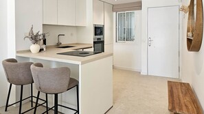 A compact kitchen with a central island, bar stools, a built-in oven, and a window with decorative glass. - Beautiful apartment with pool & sea views (Mijas Costa)