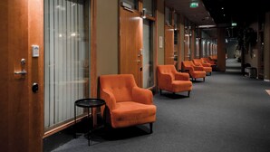 Un pasillo de hotel con filas de sillones anaranjados y puertas de madera, cada una con un número.