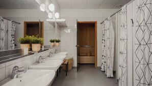 Un baño moderno con varios lavamanos, zona de ducha y sauna de madera.