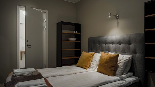 Un dormitorio con cama, almohadas, una mesita de noche, un armario y una puerta.