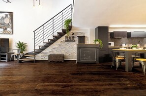 A modern kitchen with a stone wall, a staircase with a metal railing, and a bar area with a vintage sign. - Luxury Loft in Campo de' Fiori (Roma)