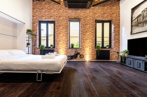 A bedroom with a brick wall, a bed, a motorcycle, and a TV. - Luxury Loft in Campo de' Fiori (Roma)