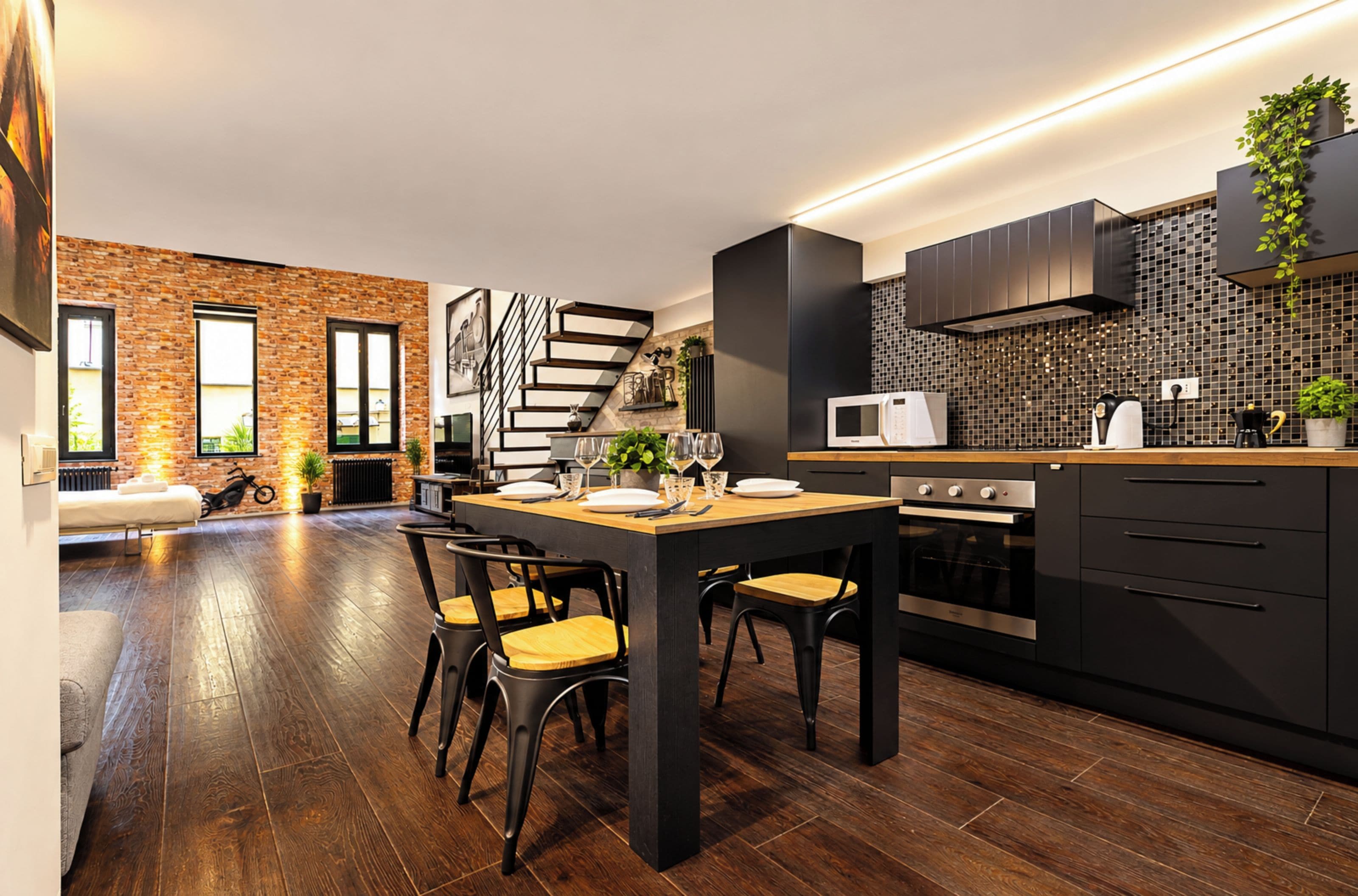 A modern kitchen with dark cabinetry, a wooden dining table, and a built-in oven.