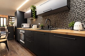 A modern kitchen with black cabinetry, a wooden countertop, a built-in oven, a microwave, a kettle, and a backsplash with small square tiles. - Luxury Loft in Campo de' Fiori (Roma)