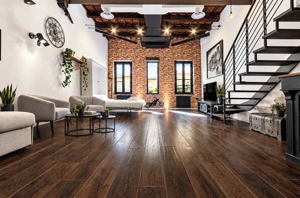 A modern living room with a brick wall, wooden flooring, and a staircase. - Luxury Loft in Campo de' Fiori (Roma)
