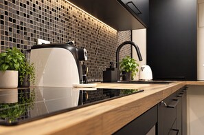 A modern kitchen with a black tiled backsplash, a stainless steel range hood, a white electric kettle, and a wooden countertop. - Luxury Loft in Campo de' Fiori (Roma)