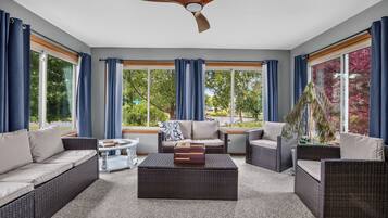 A sunroom with wicker furniture, large windows, and a ceiling fan.