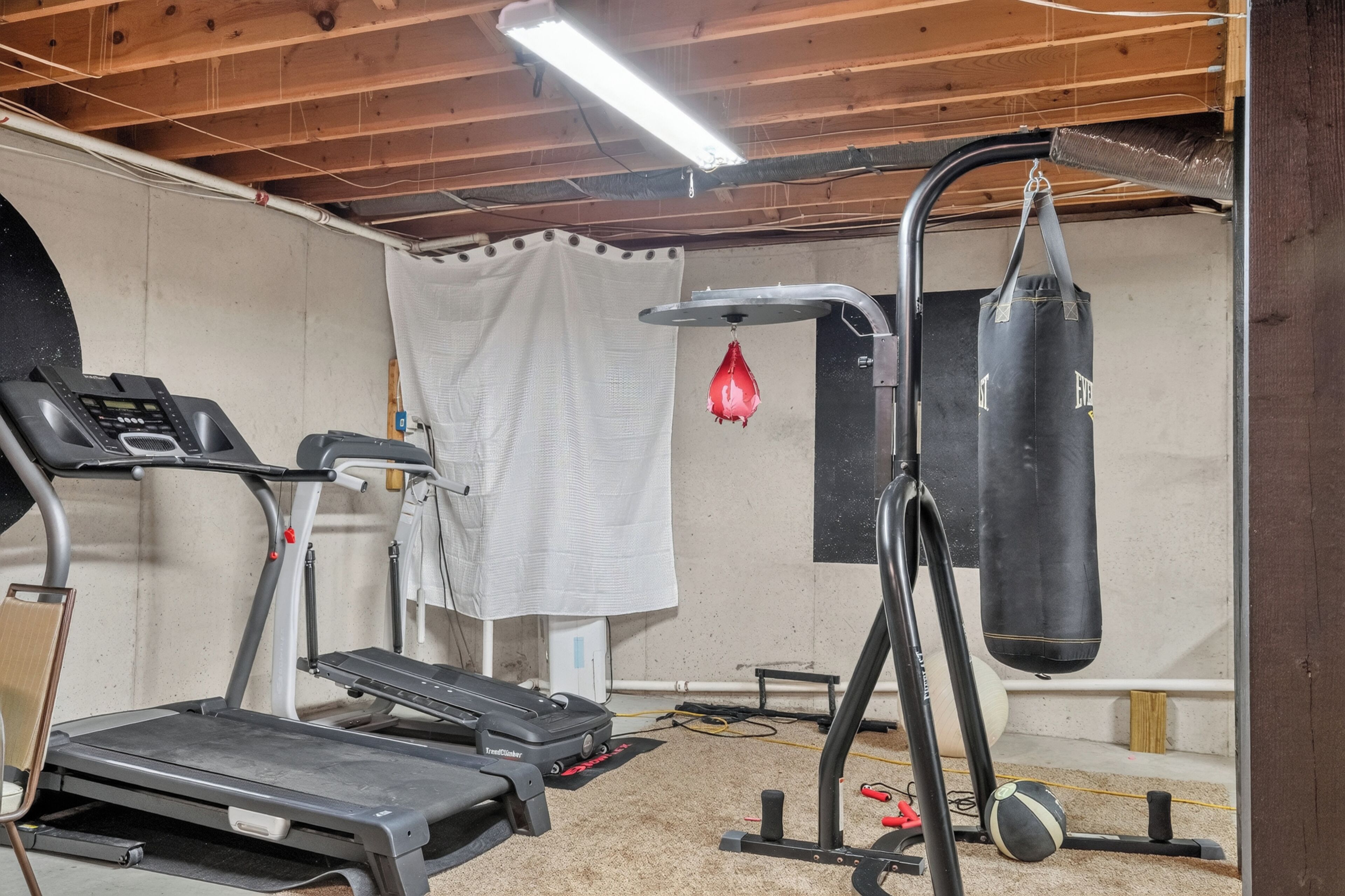 Un gimnasio en casa con cinta de correr, elíptica, saco de boxeo y banco de pesas.