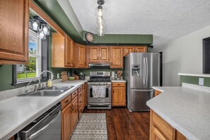 A kitchen with wooden cabinets, stainless steel appliances, a window, and a patterned rug. - Biscayne Ln Retreat/Pool, Game Room & Wawasee Fun (Cromwell)