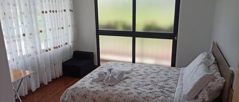 A bedroom with a bed, a window with frosted glass, a chair, and a small table.