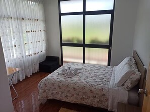 A bedroom with a bed, a window with frosted glass, a chair, and a small table. - A beautiful house in the Miraflores neighborhood of Oxapampa—very cozy and warm (Oxapampa)