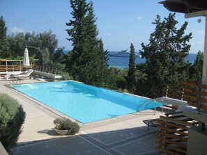 Une piscine avec vue sur la mer, entourée d’arbres et dotée d’une terrasse en bois.