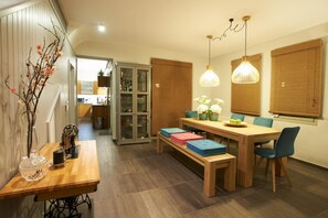 Un espace repas avec une table en bois, des bancs et des chaises. Des lampes suspendues sont fixées au plafond au-dessus de la table.
