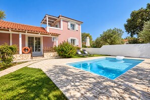 Ein zweistöckiges Haus mit Swimmingpool, einem Kiesweg und einer weißen Mauer.