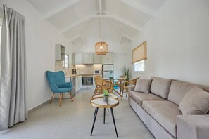 Ein modernes Wohnzimmer mit einer Couch, einem blauen Sessel, einem Esstisch mit Stühlen und einer Küche im Hintergrund.