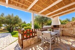 Une terrasse extérieure avec un sol en pierre, des meubles en osier et un mur en pierre intégrant un barbecue.