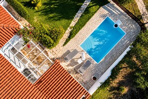 Vista aérea de um terraço com piscina, área de estar coberta e vegetação ao redor.