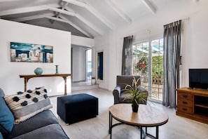 A living room with a sofa, ottoman, round table, and a television. - Villa Thalia Galini - Two Bedroom Villa, Sleeps 4 (Vassilikos)
