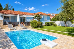 A swimming pool with a stone deck, a white fence, and a house with a red-tiled roof. - Villa Thalia Galini - Two Bedroom Villa, Sleeps 4 (Vassilikos)
