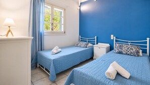 Une chambre avec deux lits, une fenêtre avec des rideaux, une table de chevet avec une lampe et un mur peint en bleu.