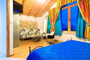 Ein Schlafzimmer mit einem Bett, einem Sessel, einer Couch und einem Fenster mit Vorhängen.