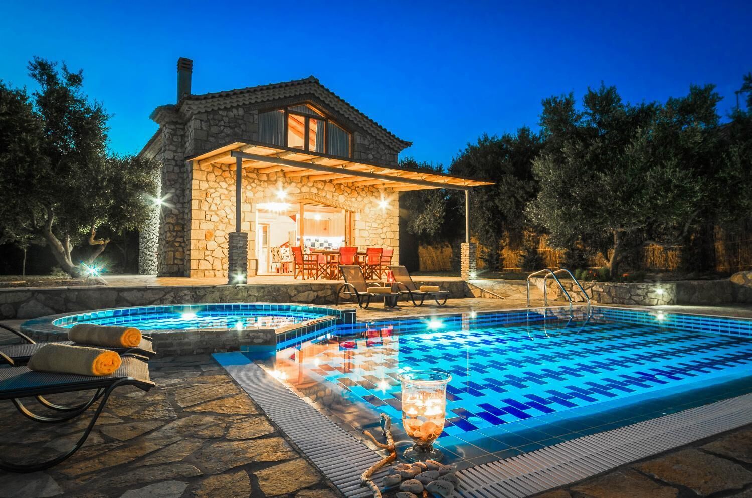 Une maison en pierre avec une piscine, un espace salon extérieur et un patio couvert.