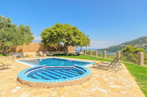 Ein Schwimmbecken mit Steinrand, umgeben von Liegestühlen und Blick aufs Meer.