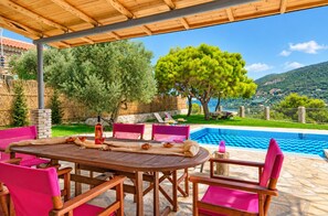 An outdoor dining area with a pool view, wooden furniture, and a stone table. - Villa Tireda Tria - Three Bedroom Villa, Sleeps 6 (Koridallos)