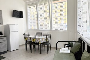 A compact living space with a kitchenette, a dining area with a table and chairs, a bed with pillows, and a TV mounted on the wall. - [Casa di Sara]Loft-6 lits-Air conditioning (La Spezia)