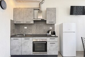 Een moderne keuken met grijze kastjes, een roestvrijstalen oven, een ingebouwde magnetron en een witte koelkast.