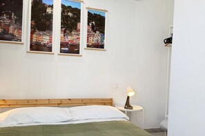 Een slaapkamer met een bed, een nachtkastje en drie ingelijste foto’s van een kustplaats.
