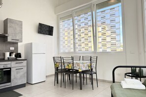 A compact kitchen with a refrigerator, stove, and microwave. There is a dining table with chairs and a bed with a green bedspread. - [Casa di Sara]Loft-6 lits-Air conditioning (La Spezia)