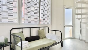 Ein Zimmer mit einem Bett, einem kleinen Tisch mit einem Kaktus und einem Fenster mit Jalousien.