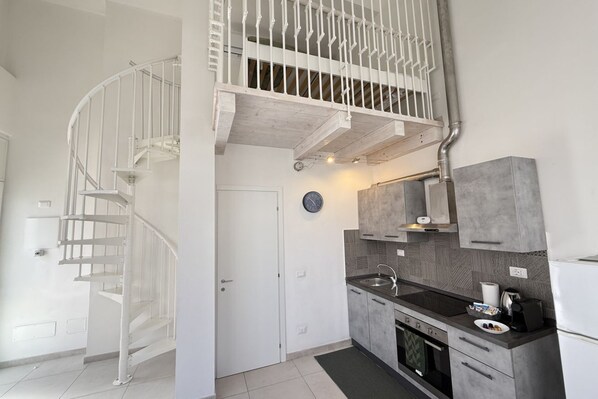 Een moderne keuken met een inbouwoven, een spoelbak en een fornuis. Een witte spiraaltrap leidt naar een hoger niveau.