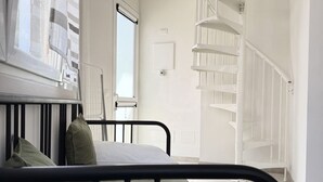 Ein Schlafzimmer mit einem Bett, einem Fenster, einer weißen Tür und einer weißen Wendeltreppe.