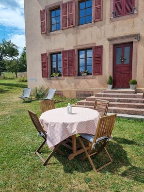Ein Gebäude mit einer roten Tür, mehreren Fenstern mit Fensterläden und einer kleinen Außenberecks mit Tisch und Stühlen.