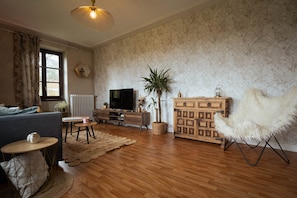 Ein Wohnzimmer mit einer Couch, Fernseher, Holzschrank und einem dekorativen Sessel.