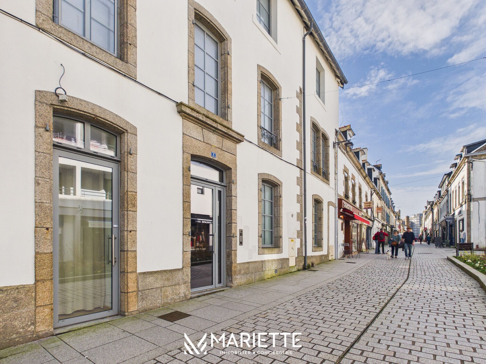 A cobblestone street lined with historic buildings, some with storefronts and signage.