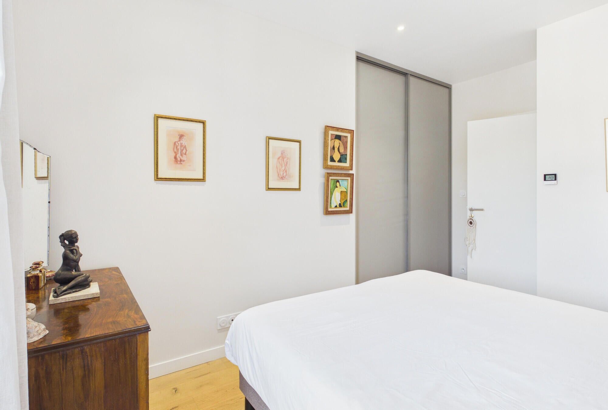 Une chambre à coucher comprenant un lit, une commode et trois œuvres d’art encadrées accrochées au mur.