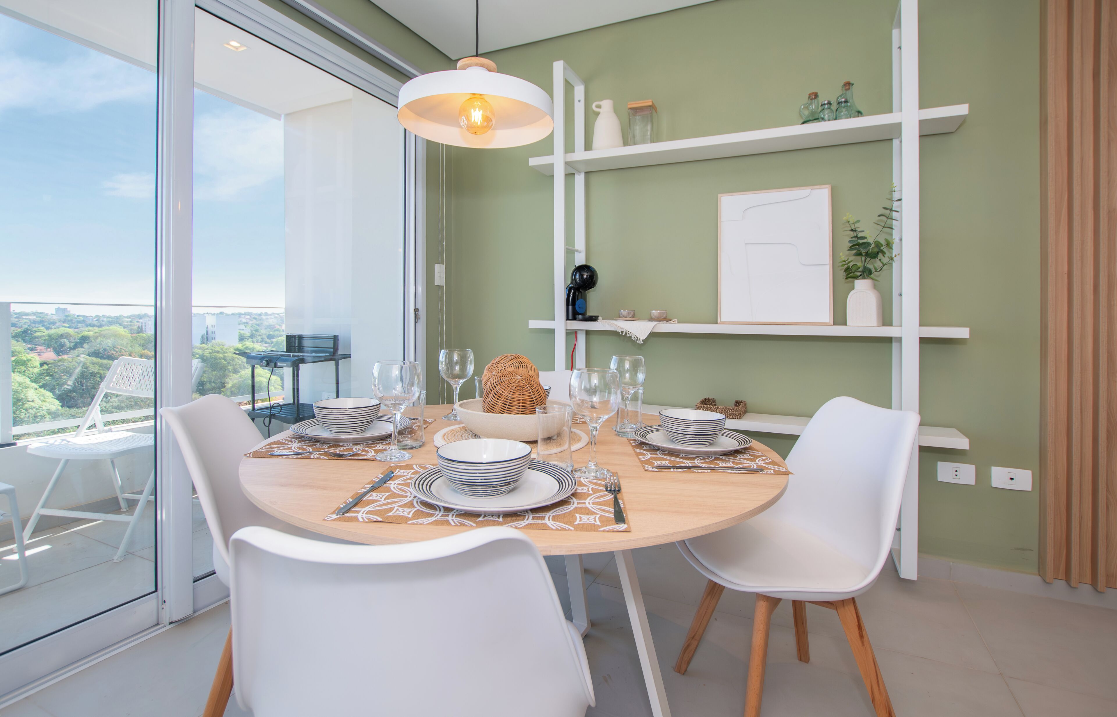 Een moderne eetruimte met een ronde tafel voor vier personen, witte stoelen en uitzicht op groen door grote ramen.