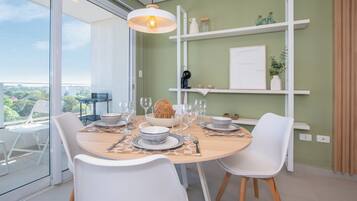 Een moderne eetruimte met een ronde tafel voor vier personen, witte stoelen en uitzicht op groen door grote ramen.