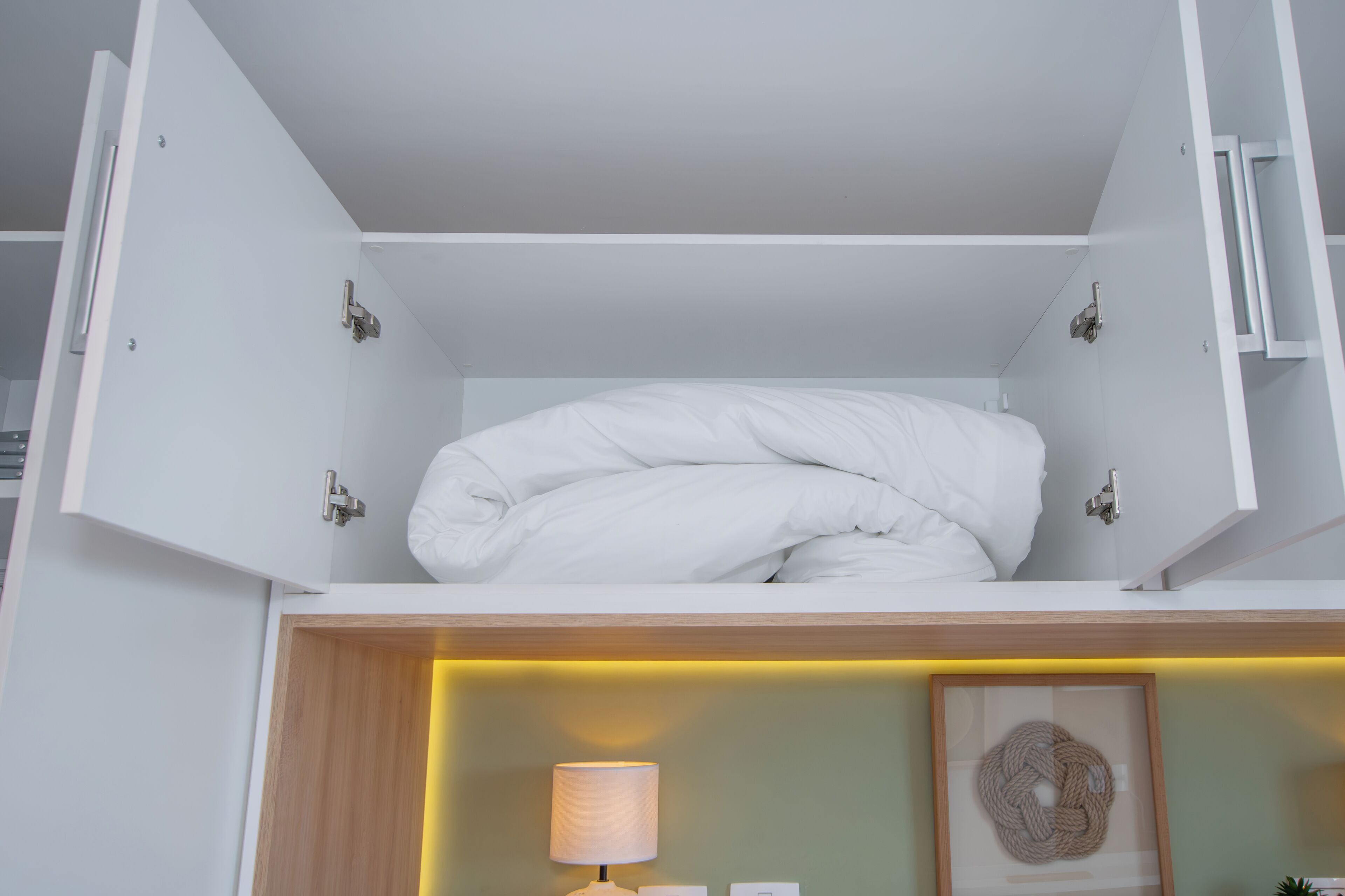 Een net opgemaakt bed in een witte kamer, met een houten hoofdeinde en een nachtkastje met een lamp.